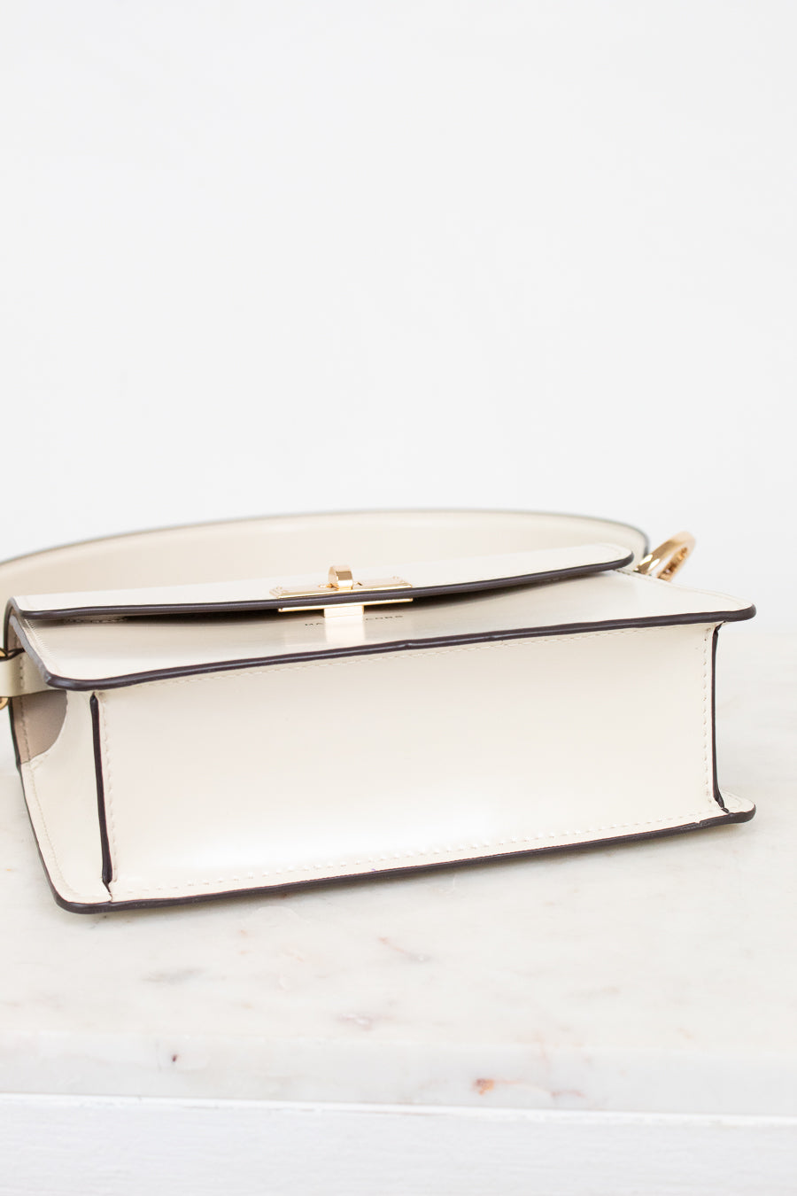 Bottom view of shoulder bag with gold accents on a white marble surface