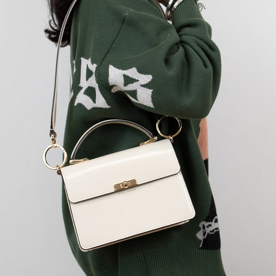 Person wearing a green sweater with white text, holding a white handbag against a plain background