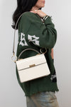 Person wearing a green sweater with white text, holding a white handbag against a plain background
