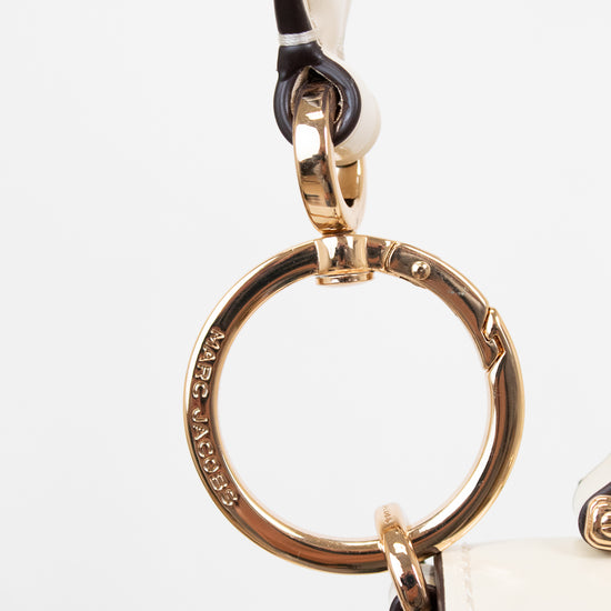 Close-up of a gold ring keychain attached to a white handbag on a light gray background