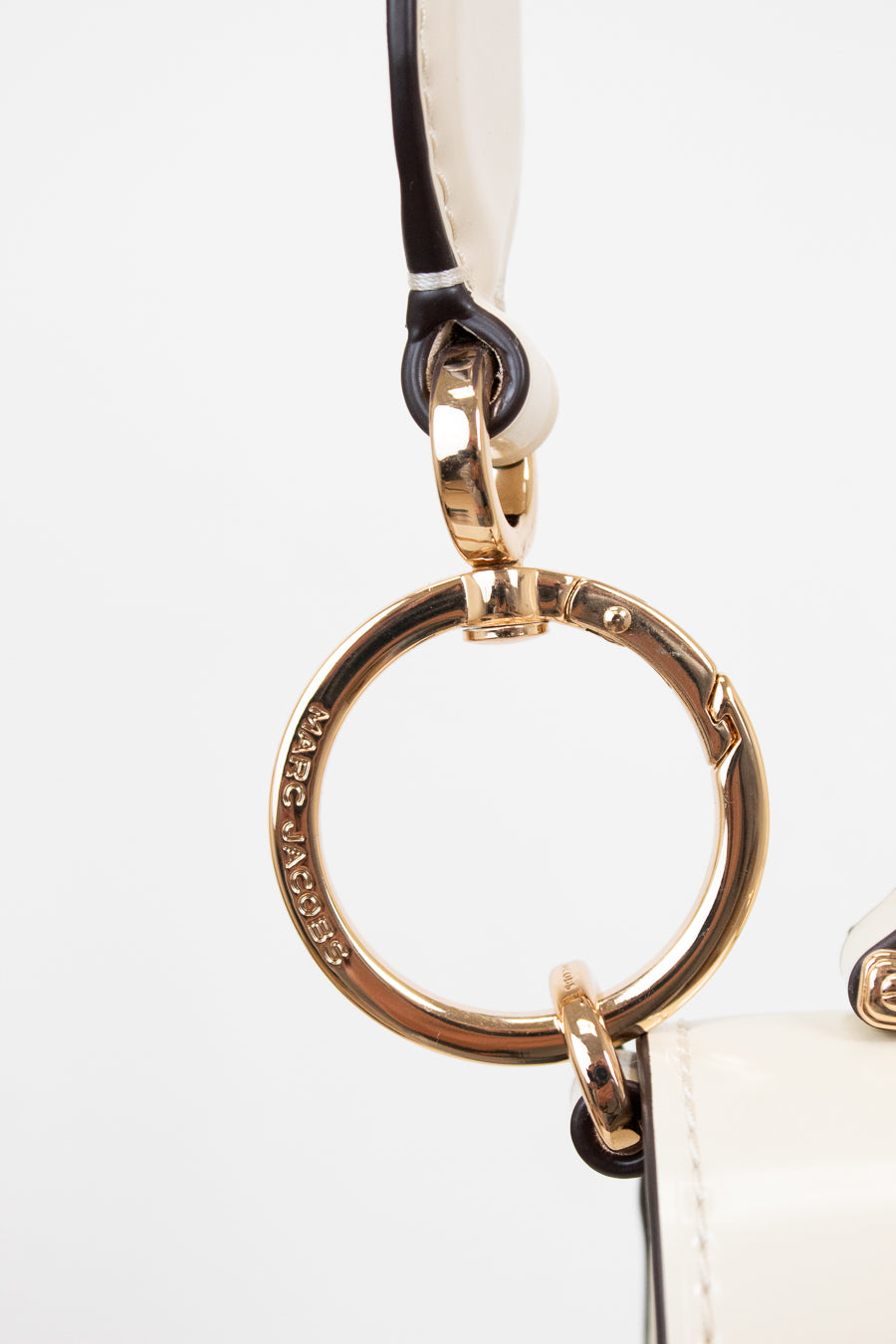 Close-up of a gold ring keychain attached to a white handbag on a light gray background