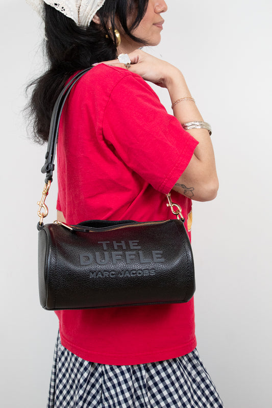 Person wearing a red shirt and black 'The Duffle' handbag with 'Marc Jacobs' branding.