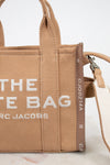 Brown handbag with 'The Tote Bag' Marc Jacobs text on a light background