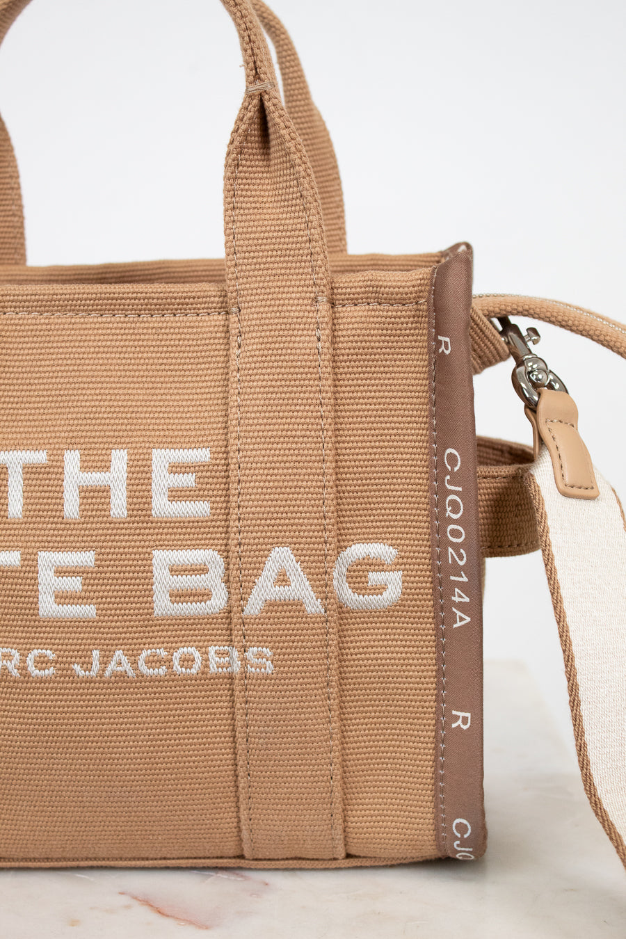 Brown handbag with 'The Tote Bag' Marc Jacobs text on a light background