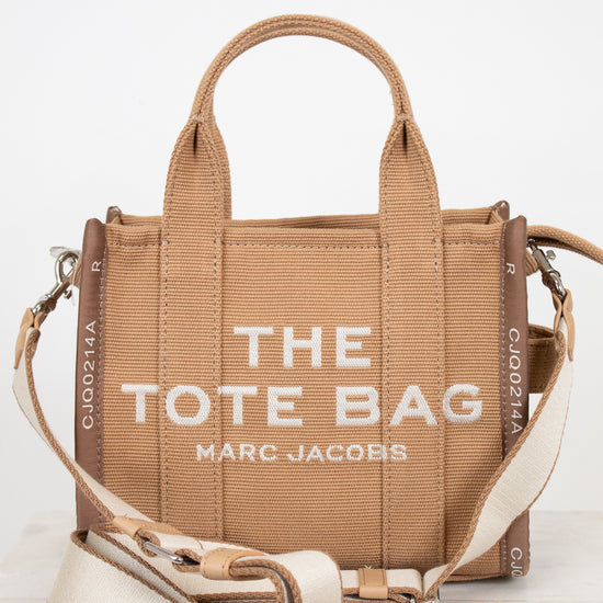 Brown tote bag with 'The Tote Bag' and 'Marc Jacobs' text on a white background
