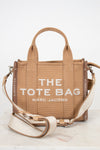 Brown tote bag with 'The Tote Bag' and 'Marc Jacobs' text on a white background