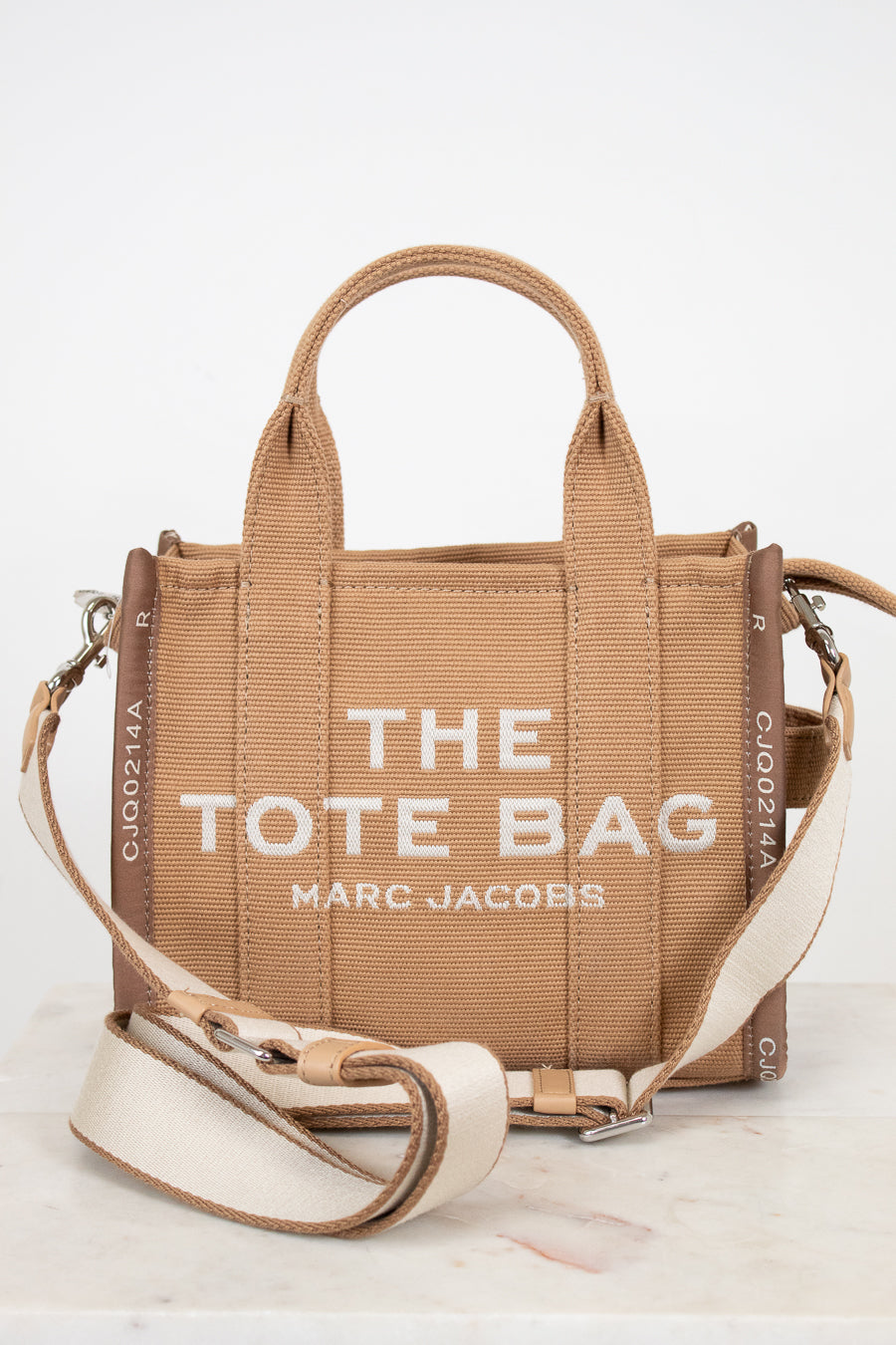 Brown tote bag with 'The Tote Bag' and 'Marc Jacobs' text on a white background