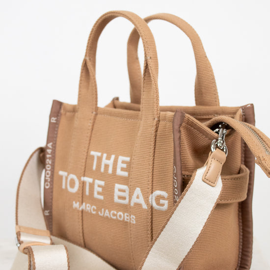 Brown tote bag with 'The Tote Bag' and 'Marc Jacobs' text on a white background