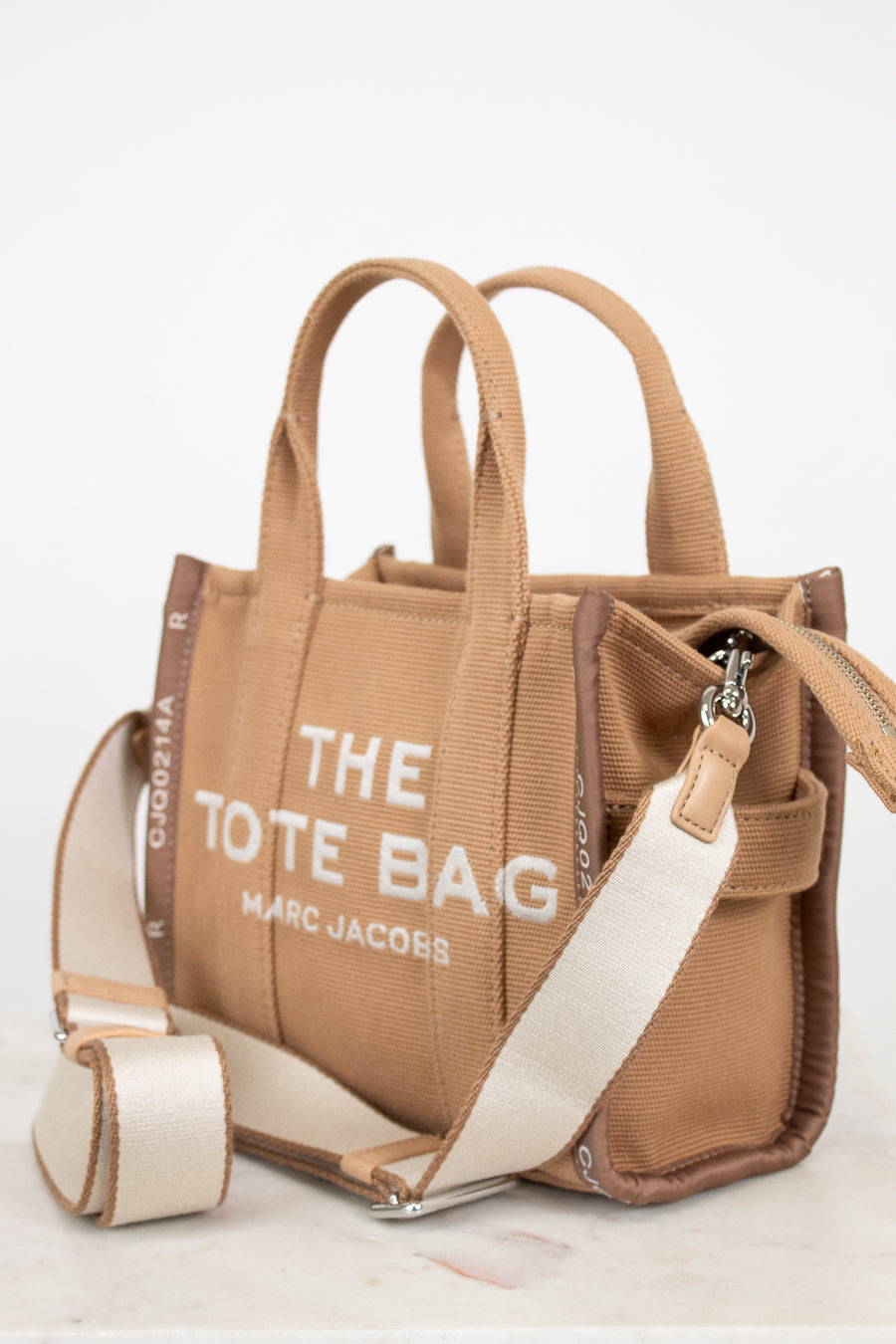 Brown tote bag with 'The Tote Bag' and 'Marc Jacobs' text on a white background