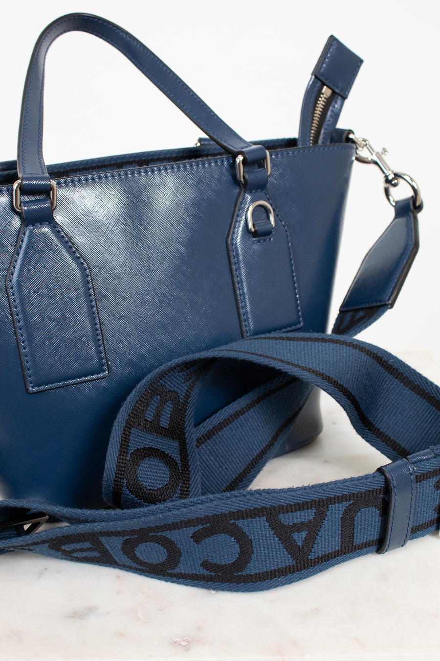 Blue handbag with a visible brand logo on the strap against a white background