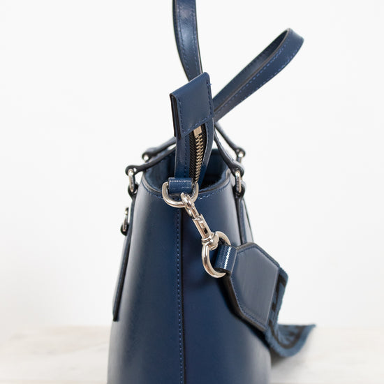 Navy blue leather handbag with a strap on a light background