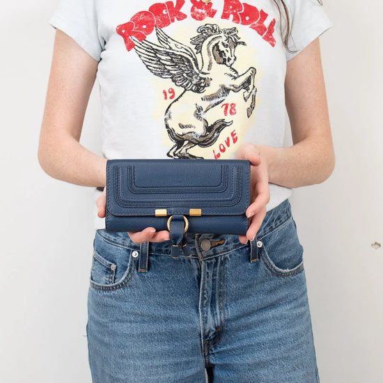 Person wearing a graphic t-shirt and holding a blue wallet against a plain background