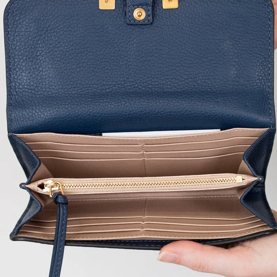 Navy blue wallet with gold accents held open by a hand on a light gray background