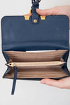 Navy blue wallet with gold accents held open by a hand on a light gray background