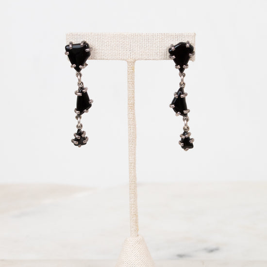 Black tiered glass earrings on a white stand with a marble background