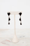 Black tiered glass earrings on a white stand with a marble background
