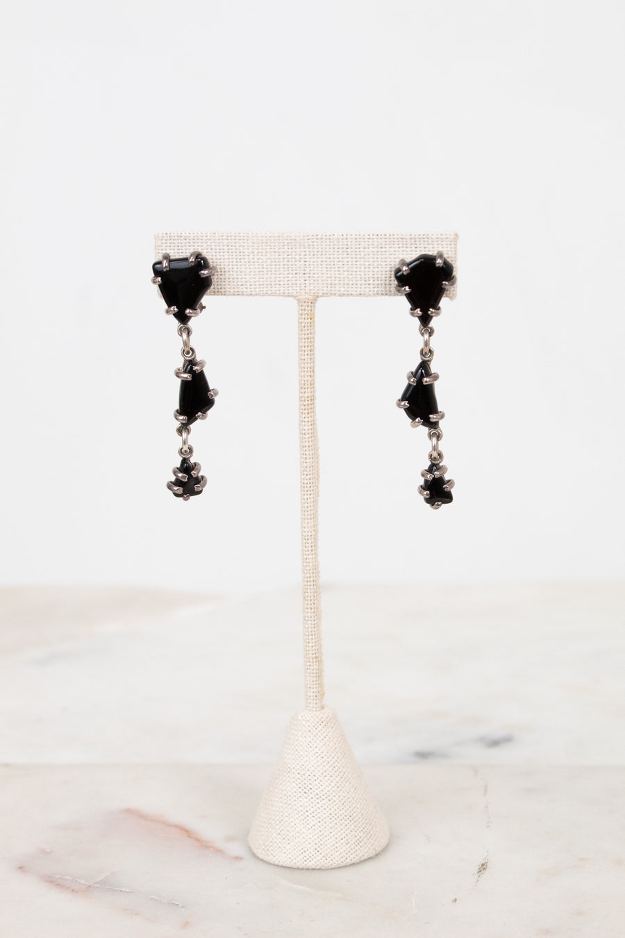 Black tiered glass earrings on a white stand with a marble background