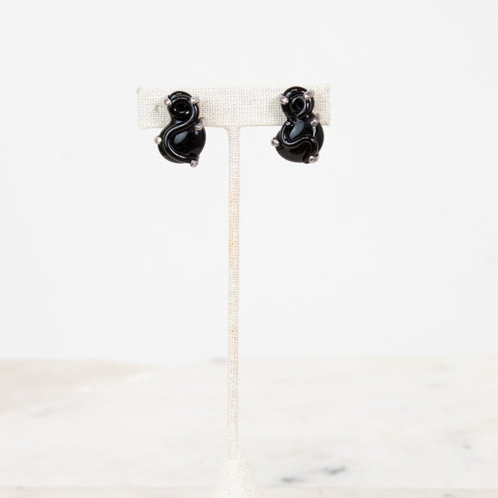 Black S-shaped glass earrings on a white stand with a white background