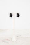 Black S-shaped glass earrings on a white stand with a white background