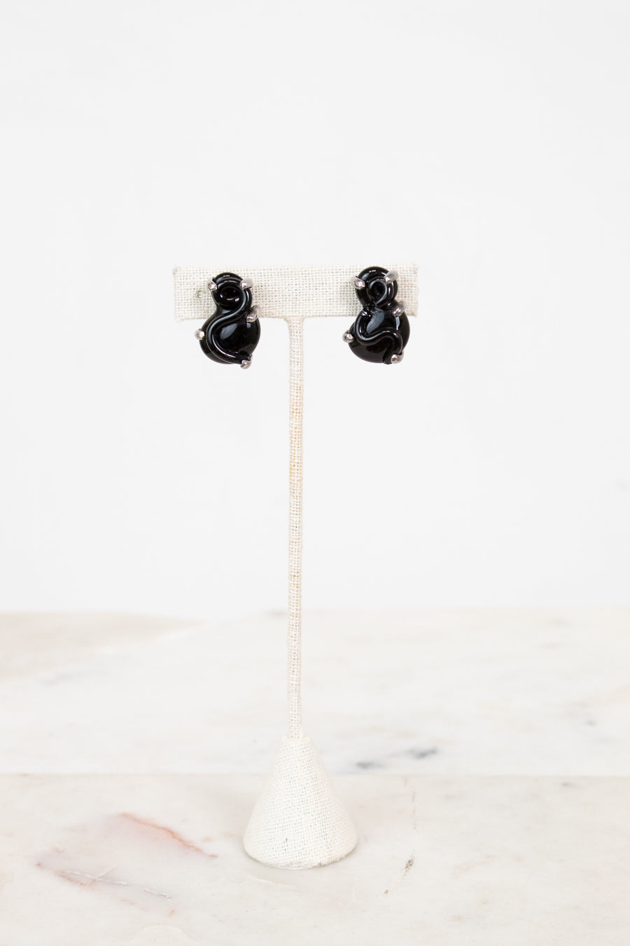 Black S-shaped glass earrings on a white stand with a white background