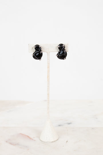 Black S-shaped glass earrings on a white stand with a white background