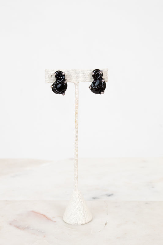 Black S-shaped glass earrings on a white stand with a white background