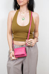 Person wearing a green top and gray pants holding a pink crossbody bag against a white background