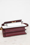 A structured leather handbag in deep burgundy saffiano with a white leather bottom panel and gold-tone hardware, displayed on a light marble surface against a white background.
