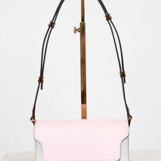 A structured shoulder bag with a light pink flap and a white body, featuring a black leather strap with gold-tone hardware, displayed on a minimalist stand.