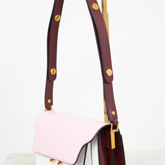A structured leather shoulder bag with a three-tone color-blocked design featuring a light pink top flap, a white lower body, and a deep burgundy side panel and strap, accented with gold-tone hardware.