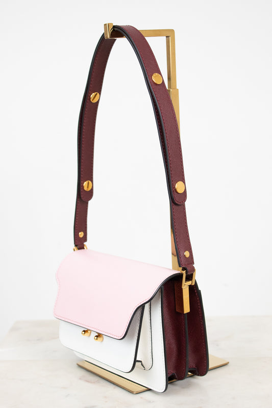 A structured leather shoulder bag with a three-tone color-blocked design featuring a light pink top flap, a white lower body, and a deep burgundy side panel and strap, accented with gold-tone hardware.