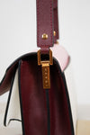 Close-up of a luxury handbag showing a deep burgundy saffiano leather strap, a gold-tone metal clasp with 'MARNI' engraved, and a soft pink leather exterior panel.