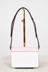 A structured rectangular handbag with a light pink top flap and white body, featuring burgundy leather shoulder straps with gold-tone hardware, displayed on a minimalist stand.