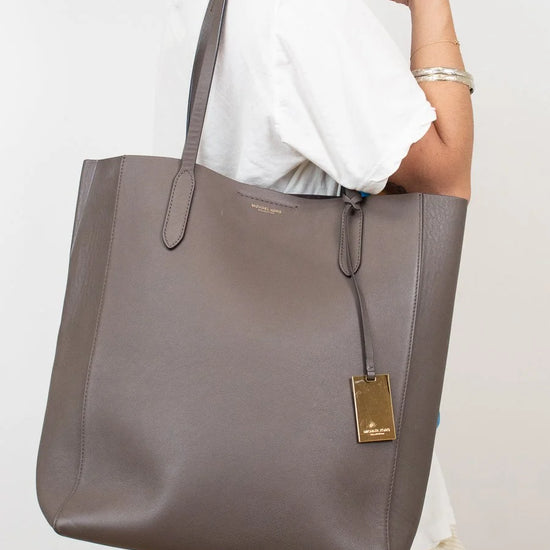 Person holding a large brown tote bag with a visible brand logo against a plain background