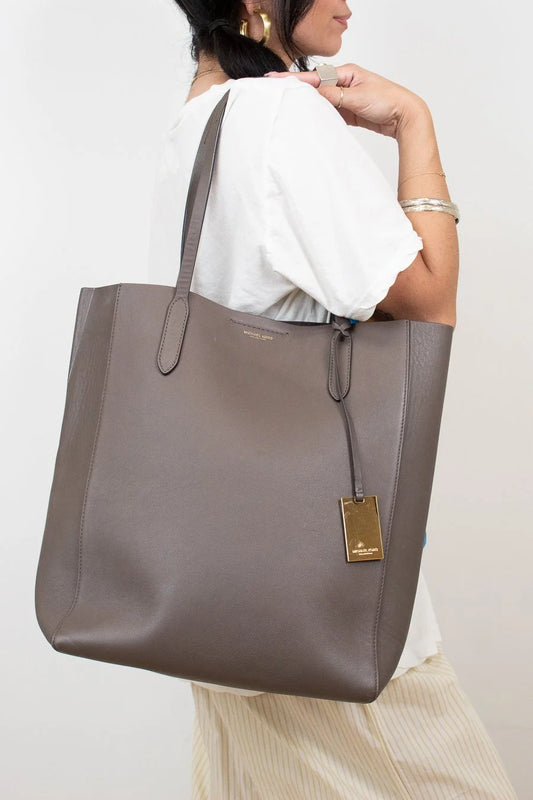 Person holding a large brown tote bag with a visible brand logo against a plain background