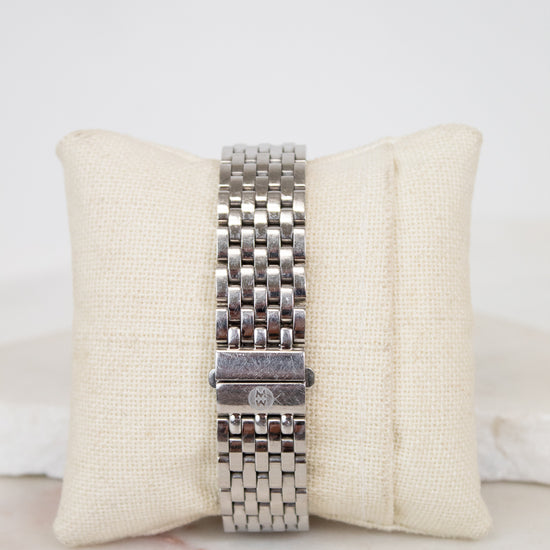 Silver watch band on a beige cushion with a white background