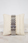 Silver watch band on a beige cushion with a white background
