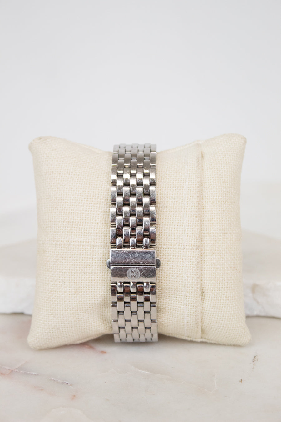 Silver watch band on a beige cushion with a white background
