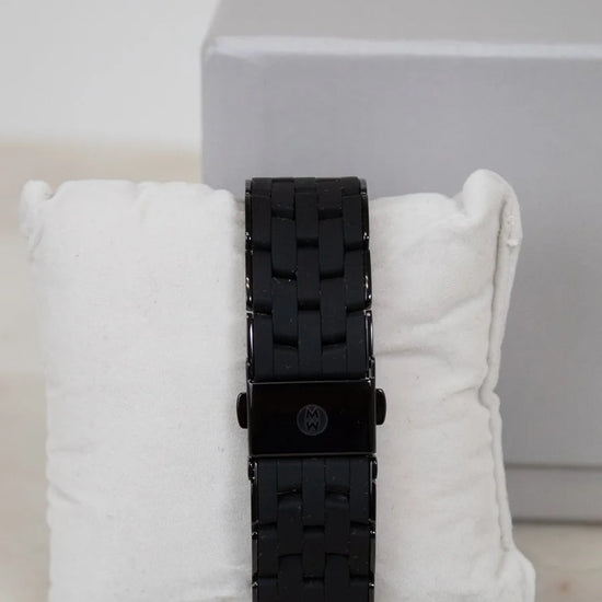 Black watch with textured strap on a white cushion against a light gray background