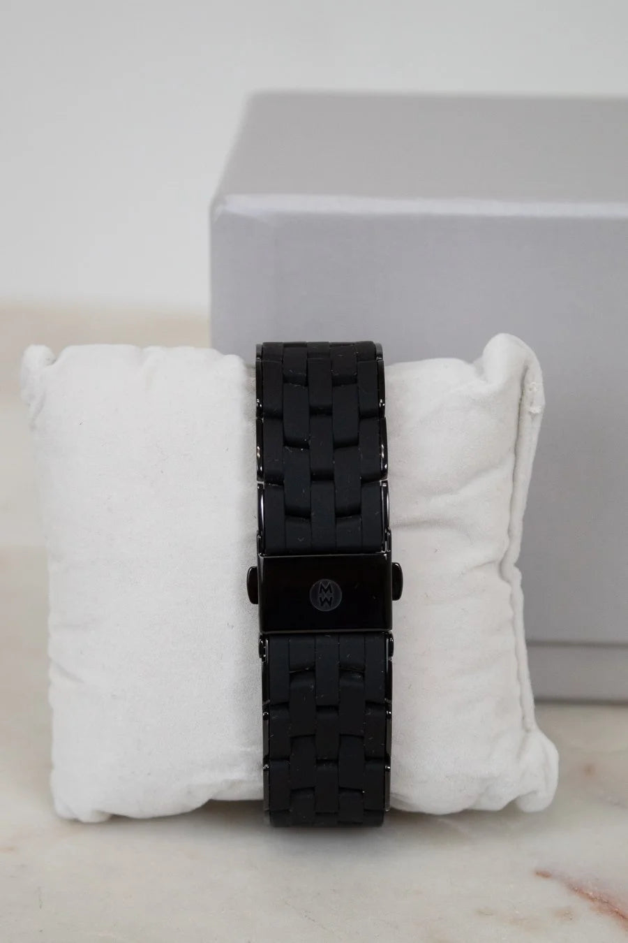Black watch with textured strap on a white cushion against a light gray background