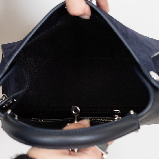 Close-up of a hand holding a navy handbag with a white background