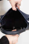 Close-up of a hand holding a navy handbag with a white background