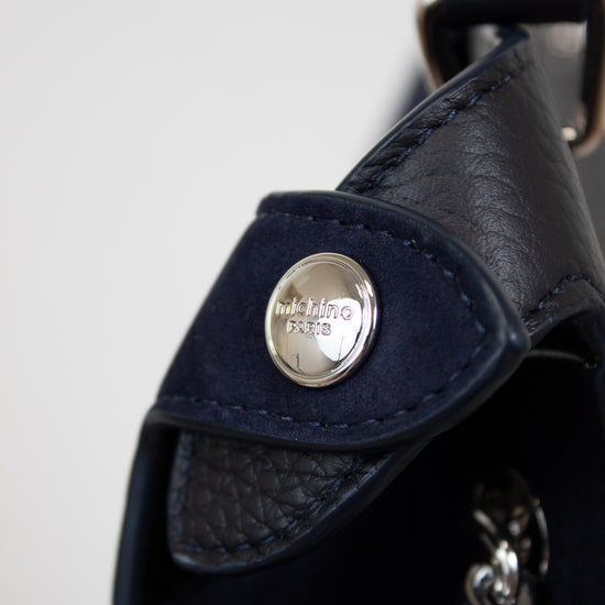 Close-up of a navy leather bag with a silver brand logo on a light gray background
