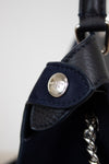 Close-up of a navy leather bag with a silver brand logo on a light gray background