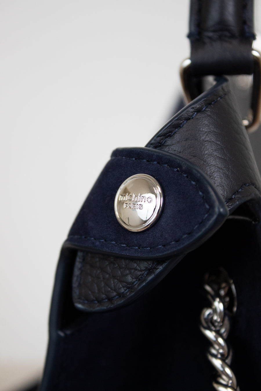 Close-up of a navy leather bag with a silver brand logo on a light gray background