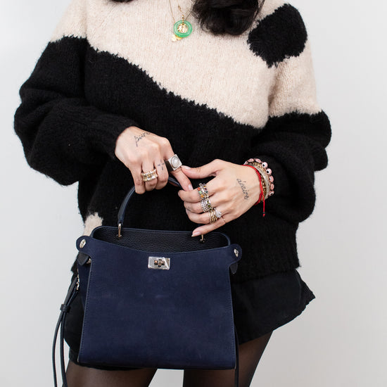 Person wearing a black and white sweater holding a navy blue handbag against a plain background