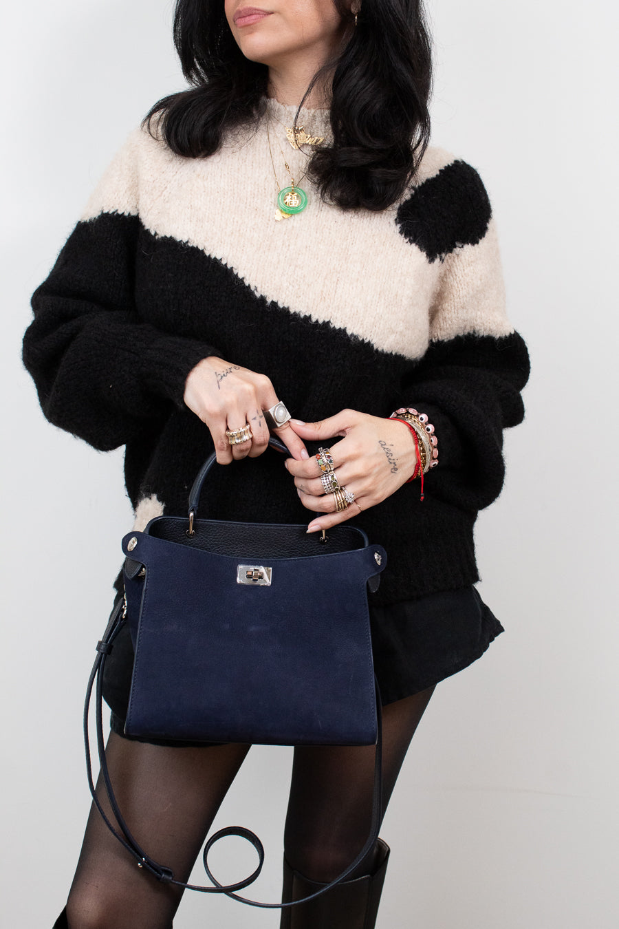 Person wearing a black and white sweater holding a navy blue handbag against a plain background