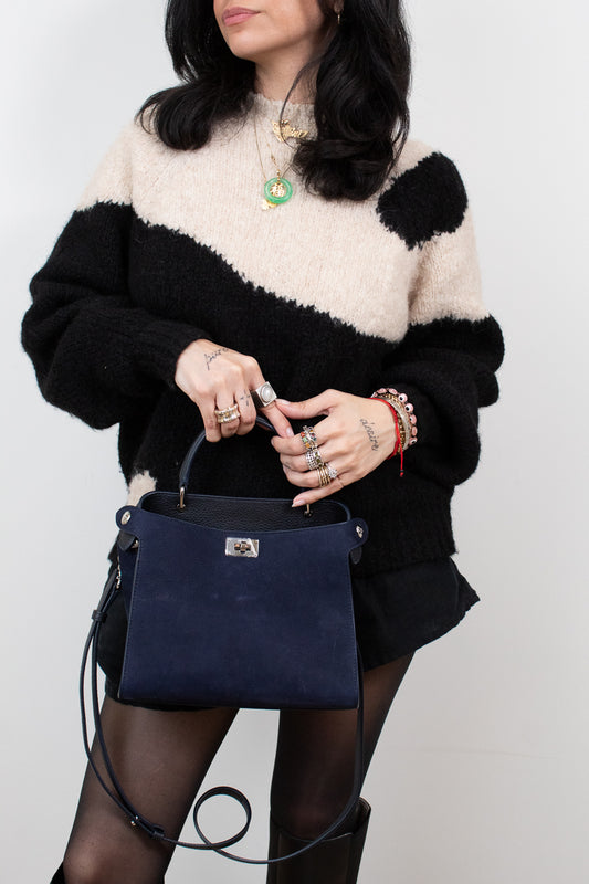 Person wearing a black and white sweater holding a navy blue handbag against a plain background