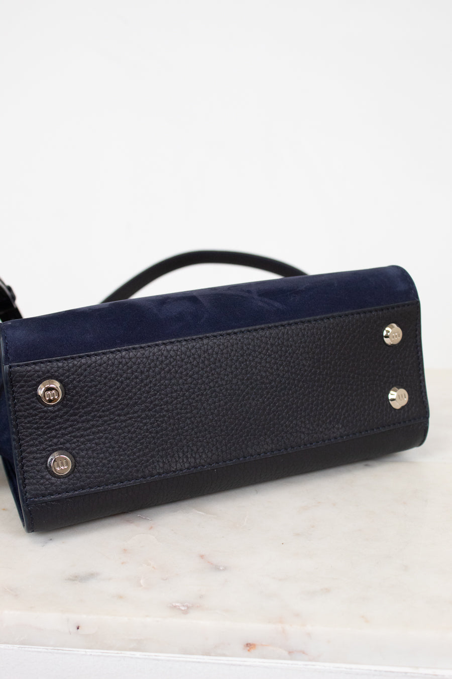 Black leather handbag with silver-tone feet on a marble surface