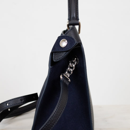 Navy blue leather bag with a chain detail strap on a light gray background